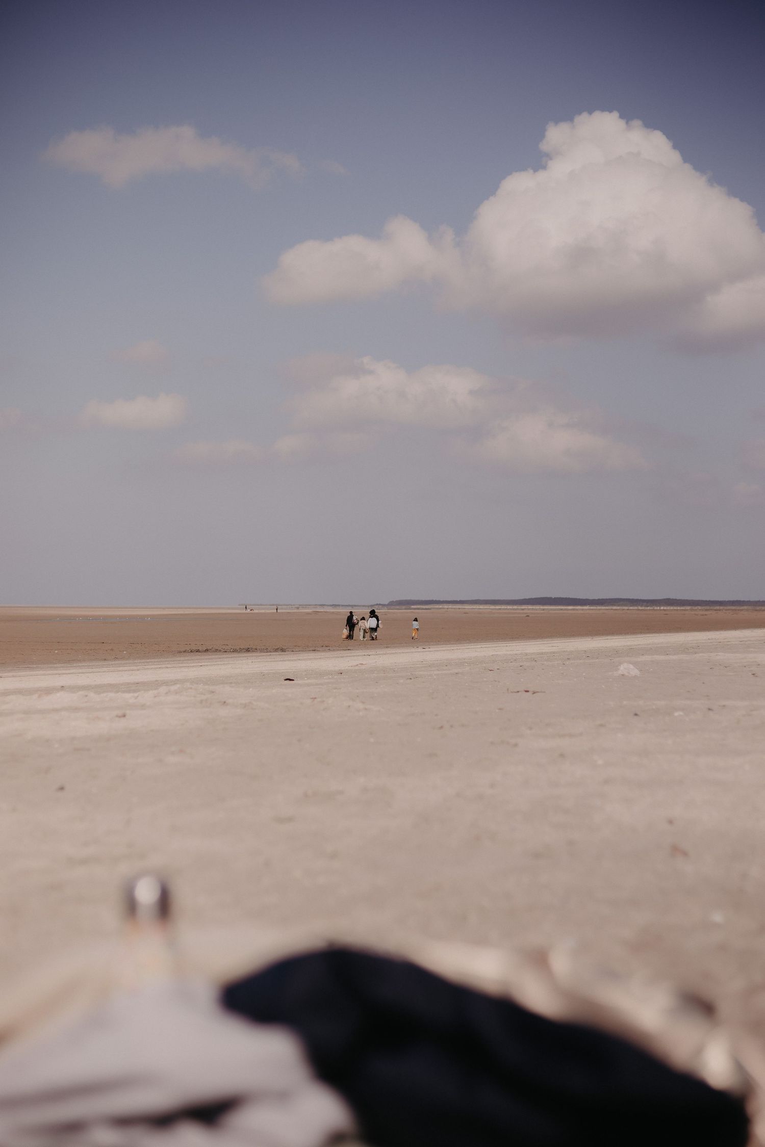 People walking on an expansive sandy beach under puffy clouds on a calm summer day.