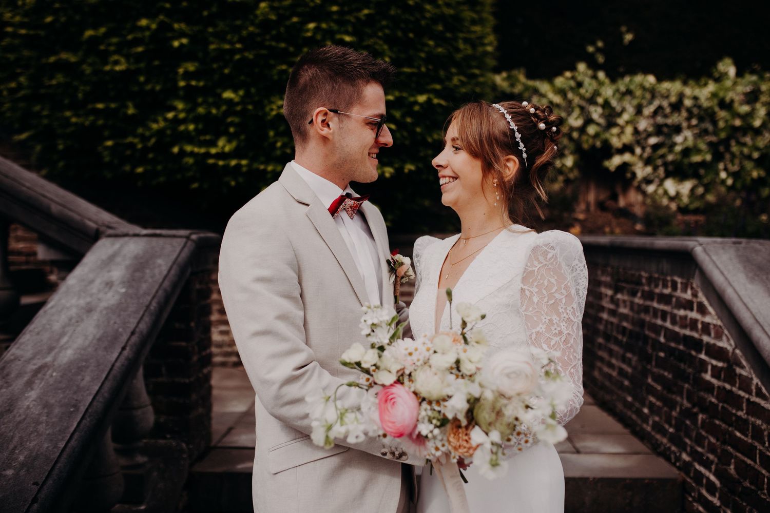 A bride and groom share an intimate moment outdoors while holding a delicate bouquet of white and pink flowers.