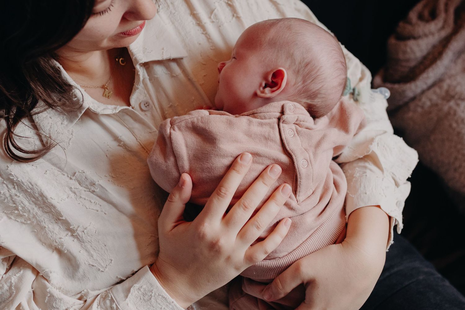 Close up of hands gently holding a sleeping newborn baby wrapped in soft fabric.