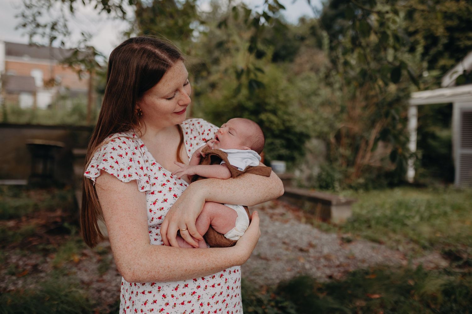 A parent in a polka dot dress holds and embraces a newborn baby in a peaceful outdoor setting.