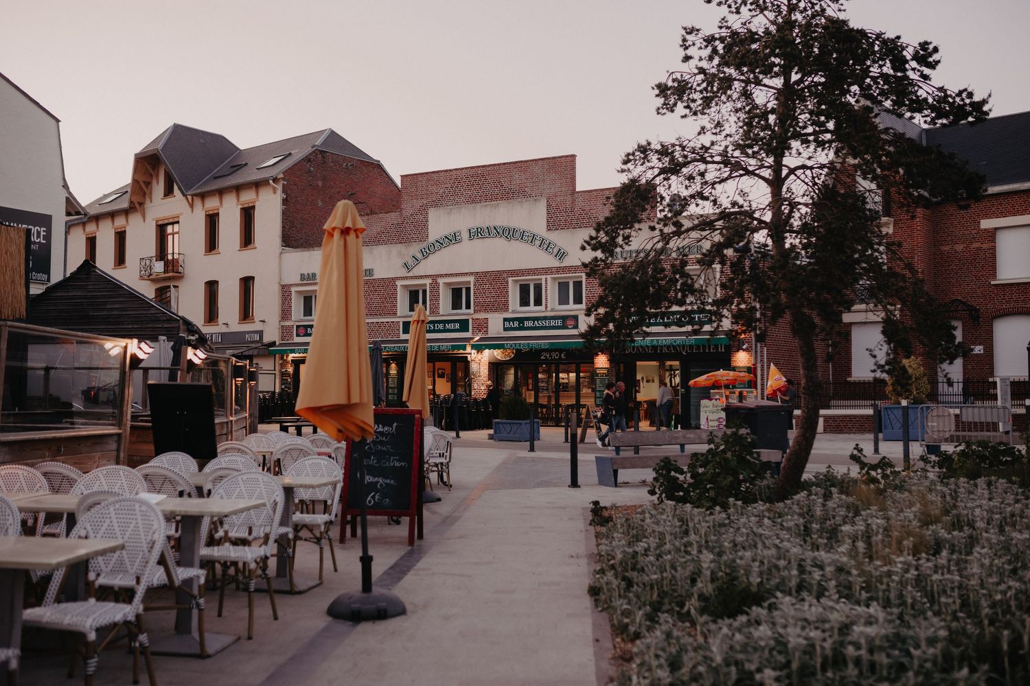 Outdoor patio seating area with white chairs in front of historic brick buildings at dusk.