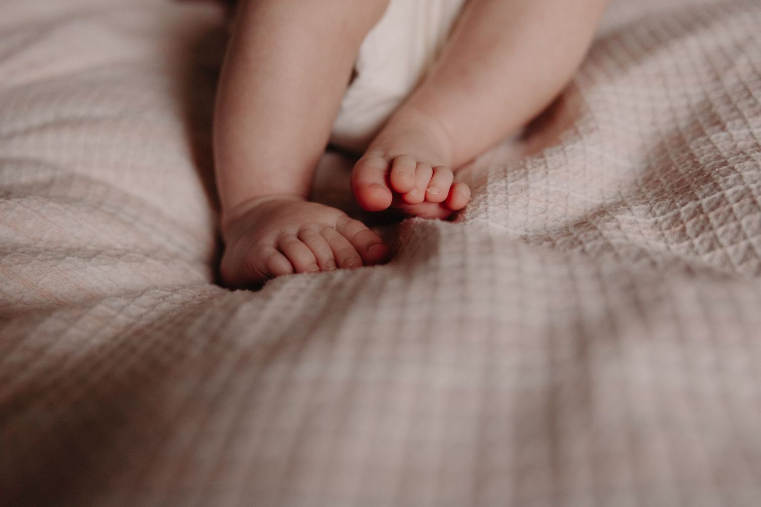 Close-up photo of tiny baby toes on soft white textured blanket in warm sepia tones.