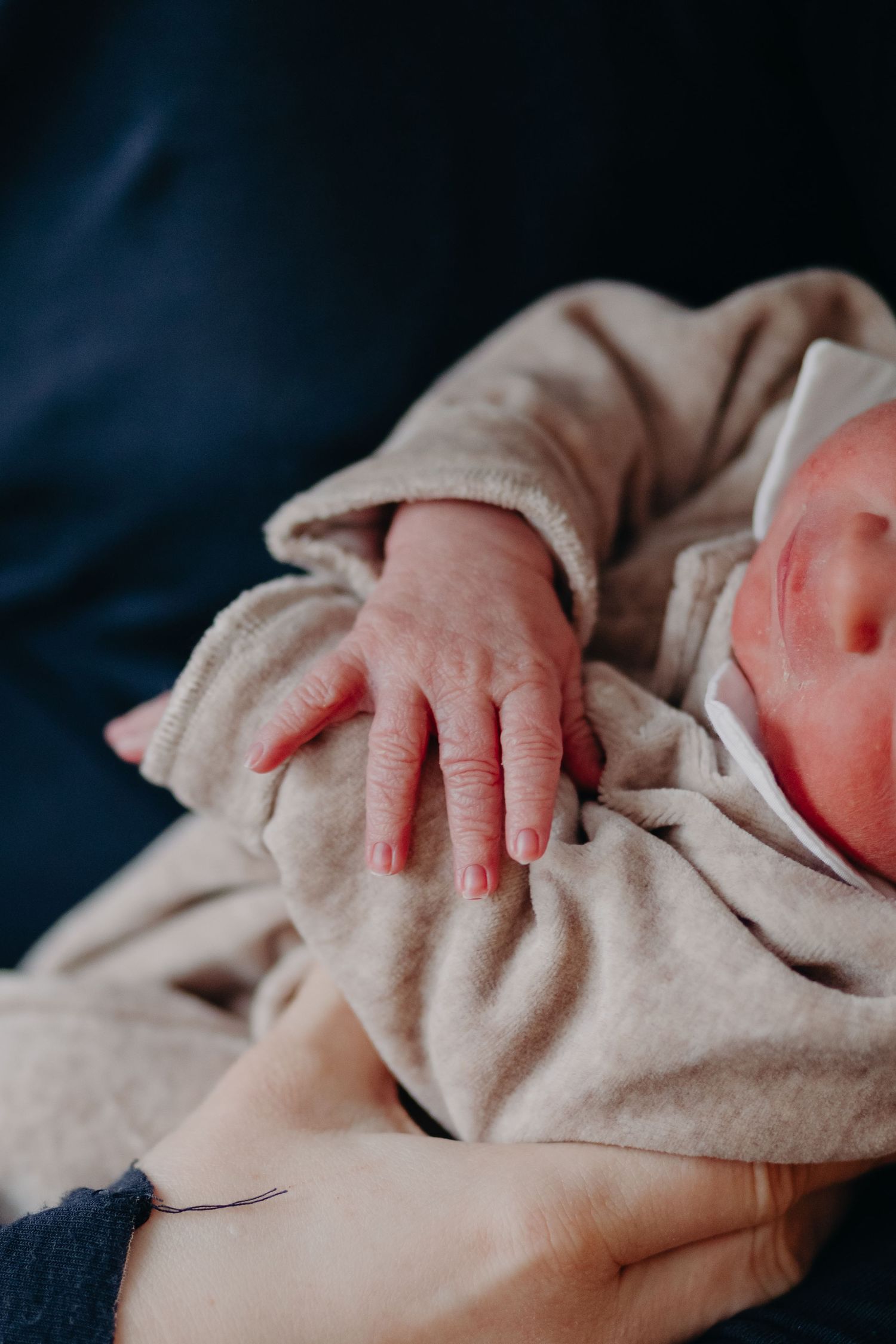 Close-up of a newborn baby's tiny hand resting on soft beige fabric against a dark blue background.