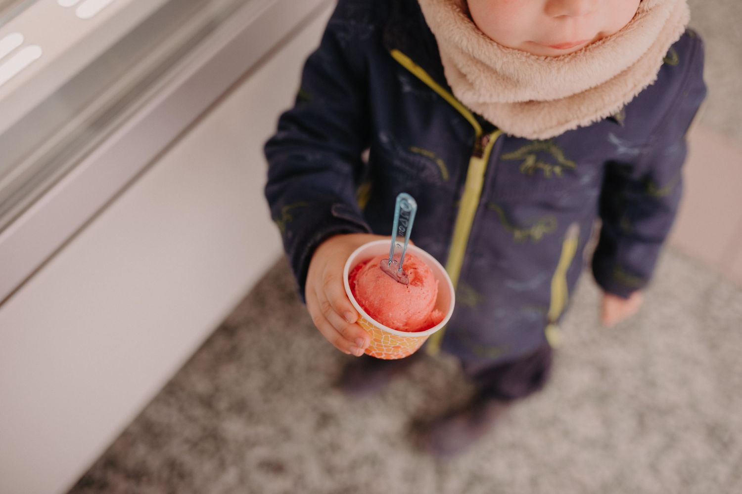 Someone in a navy jacket holds a bright red apple with a toothpick inserted in their hand against a carpeted floor.
