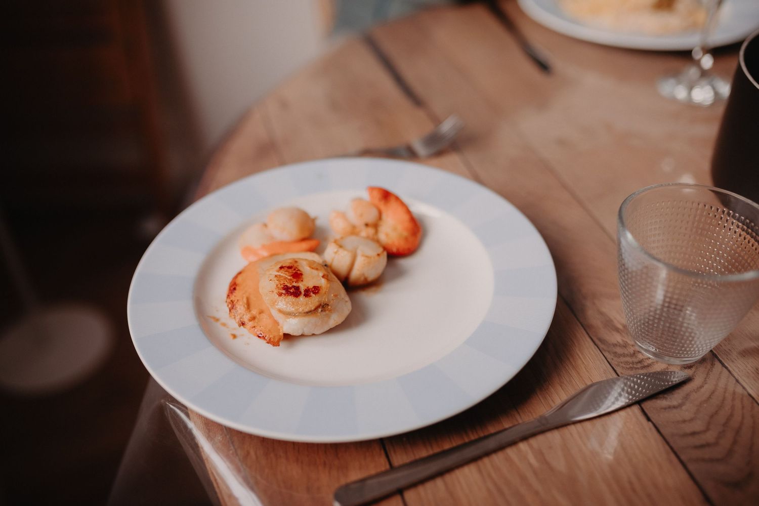 Seared scallops and shrimp served on a white plate with creamy sauce on a wooden table.