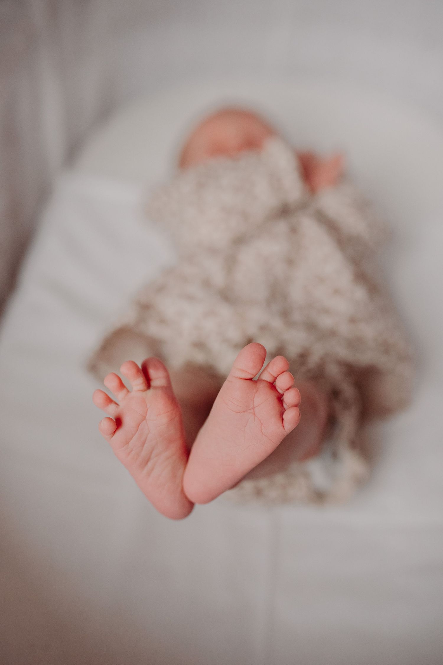 A newborn baby's tiny pink feet peek out from underneath a soft white blanket.