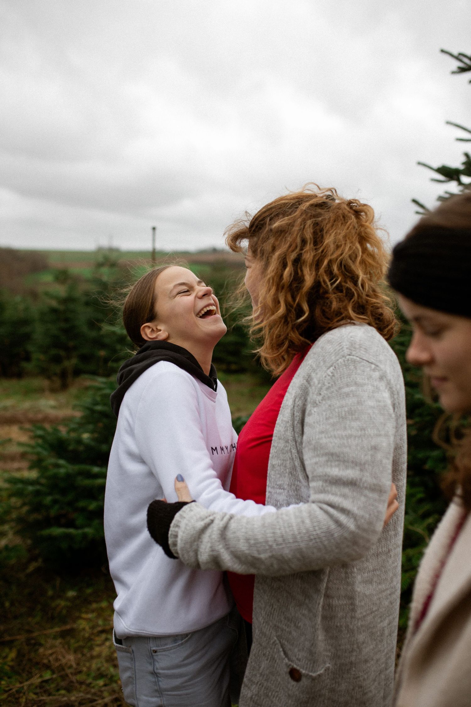 Two friends sharing a joyful moment of laughter together outdoors against a cloudy sky.