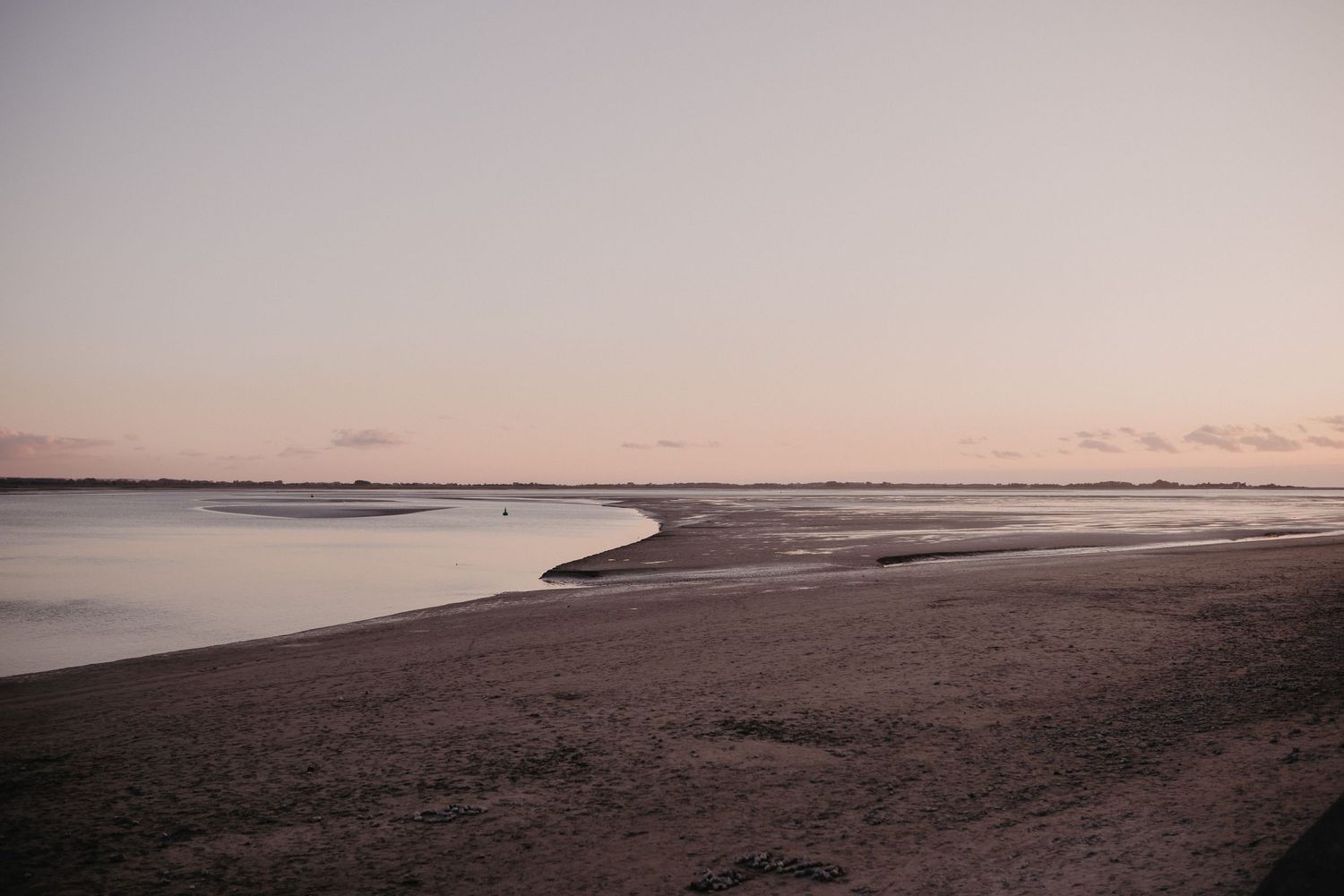 A serene coastal beach landscape at dusk with calm waters and curving shoreline stretching into the distance.
