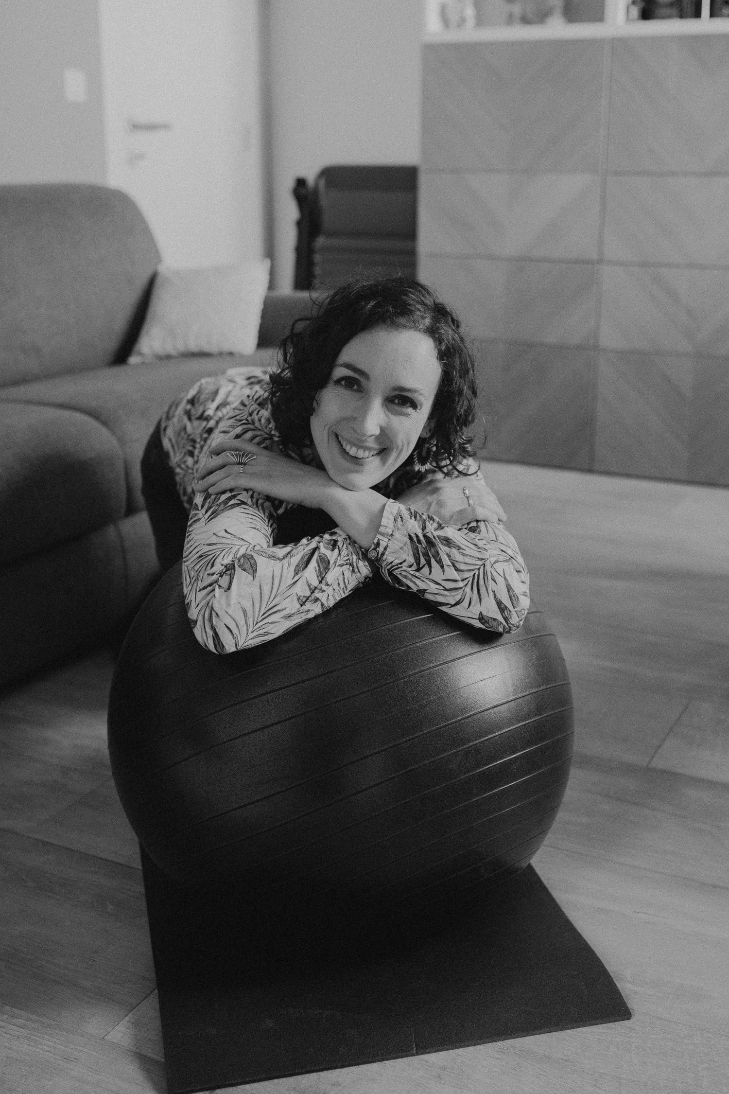 A person relaxes on a large black exercise ball in a home setting with hardwood floors and gray decor.