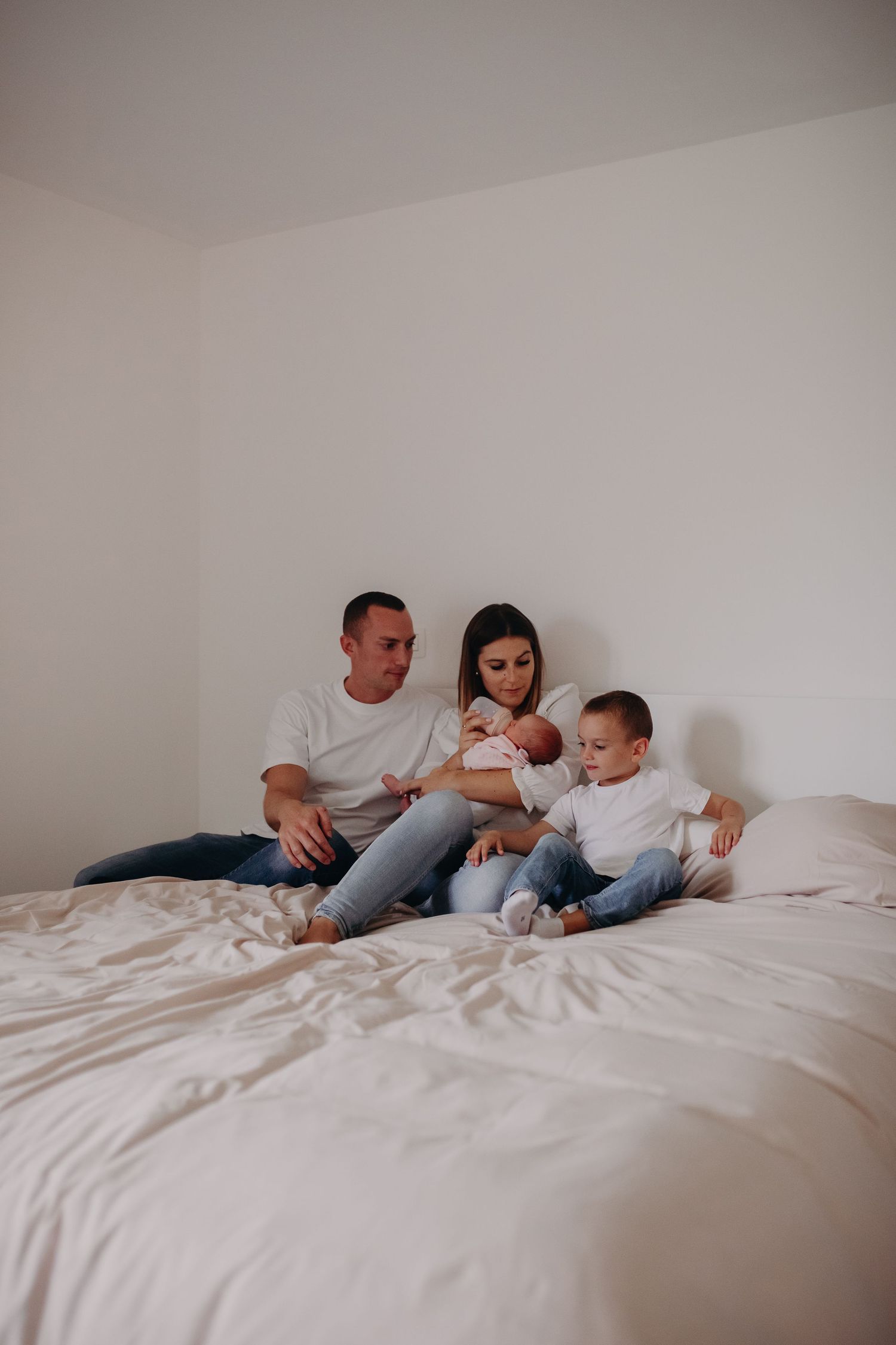 A family relaxes together on a white bed, spending quality time in a minimalist bedroom setting.