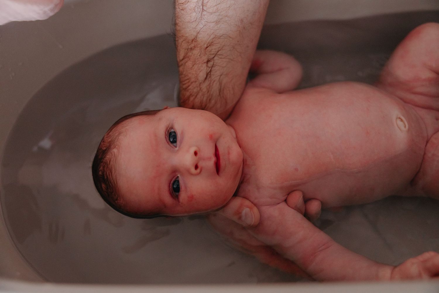 Baby getting gently bathed in warm water with supporting hands.