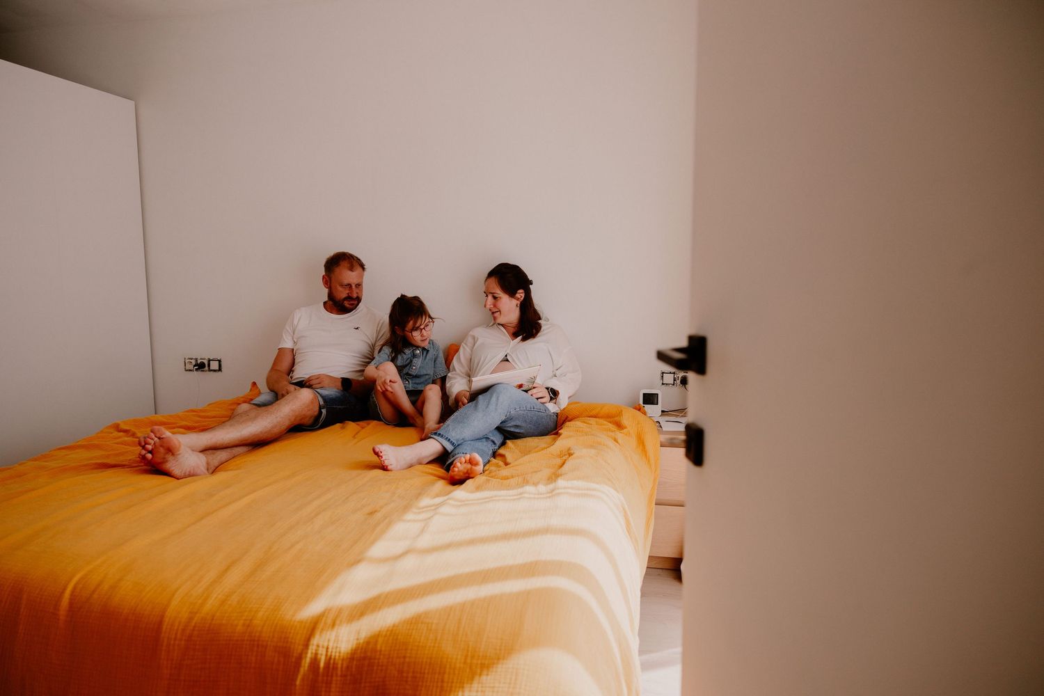 Family of three relaxing together on a yellow bed in a bright, modern bedroom.