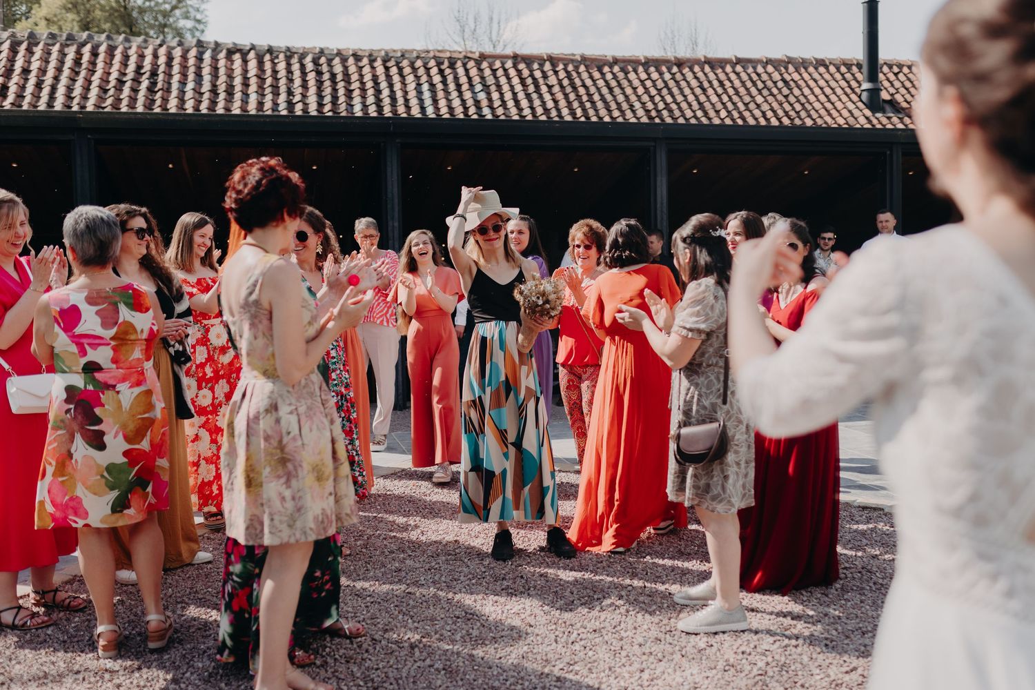 A gathering of people wearing colorful dresses and outfits stand together at an outdoor courtyard event.