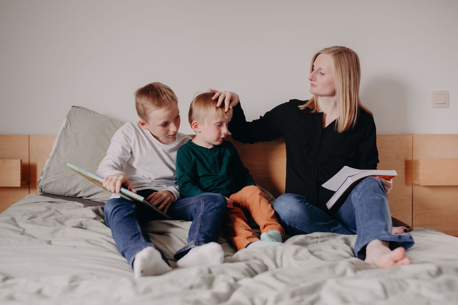 Family sitting together on bed reading books surrounded by moving boxes in their new home.