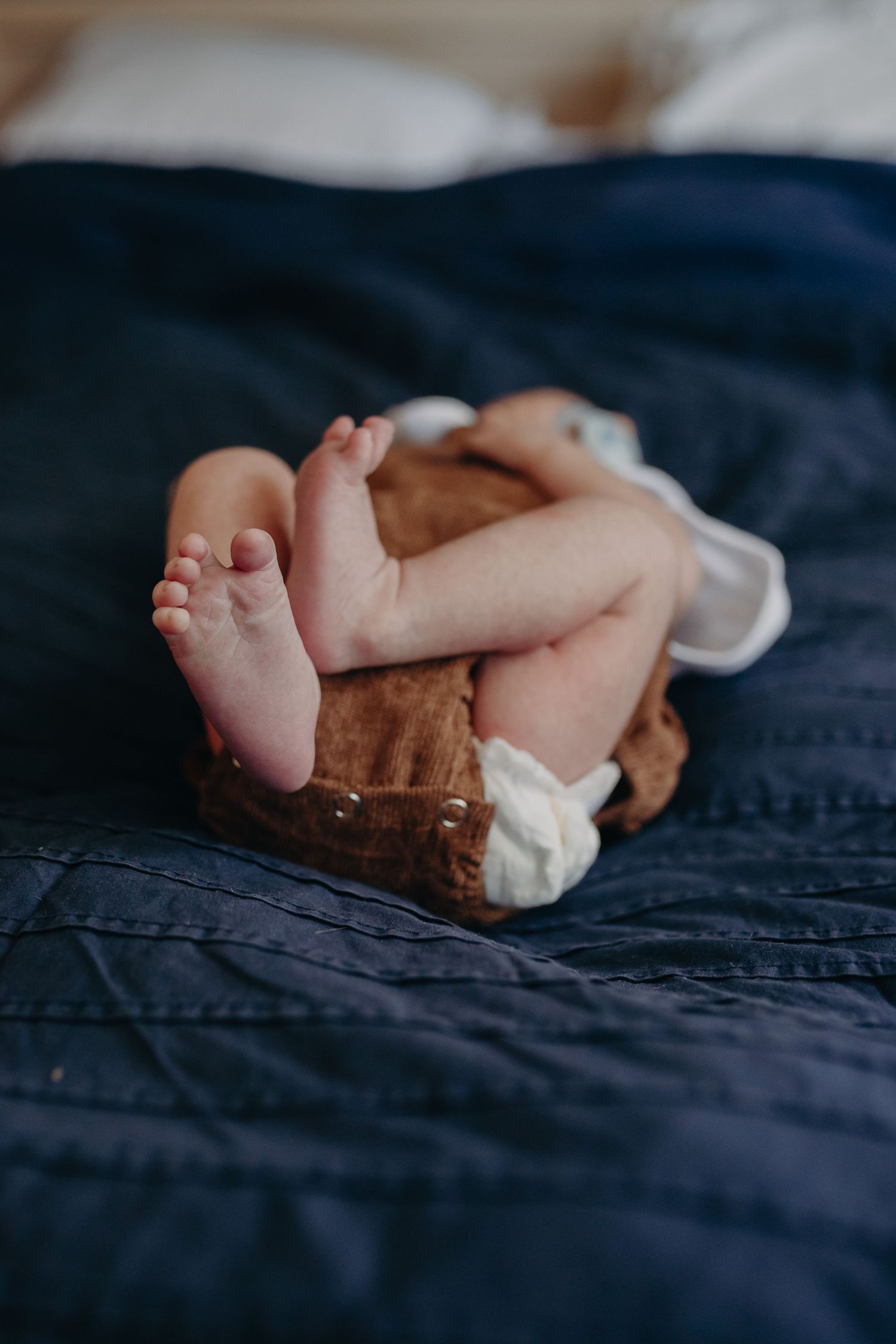Close-up of tiny baby feet and legs resting on dark blue bedding.