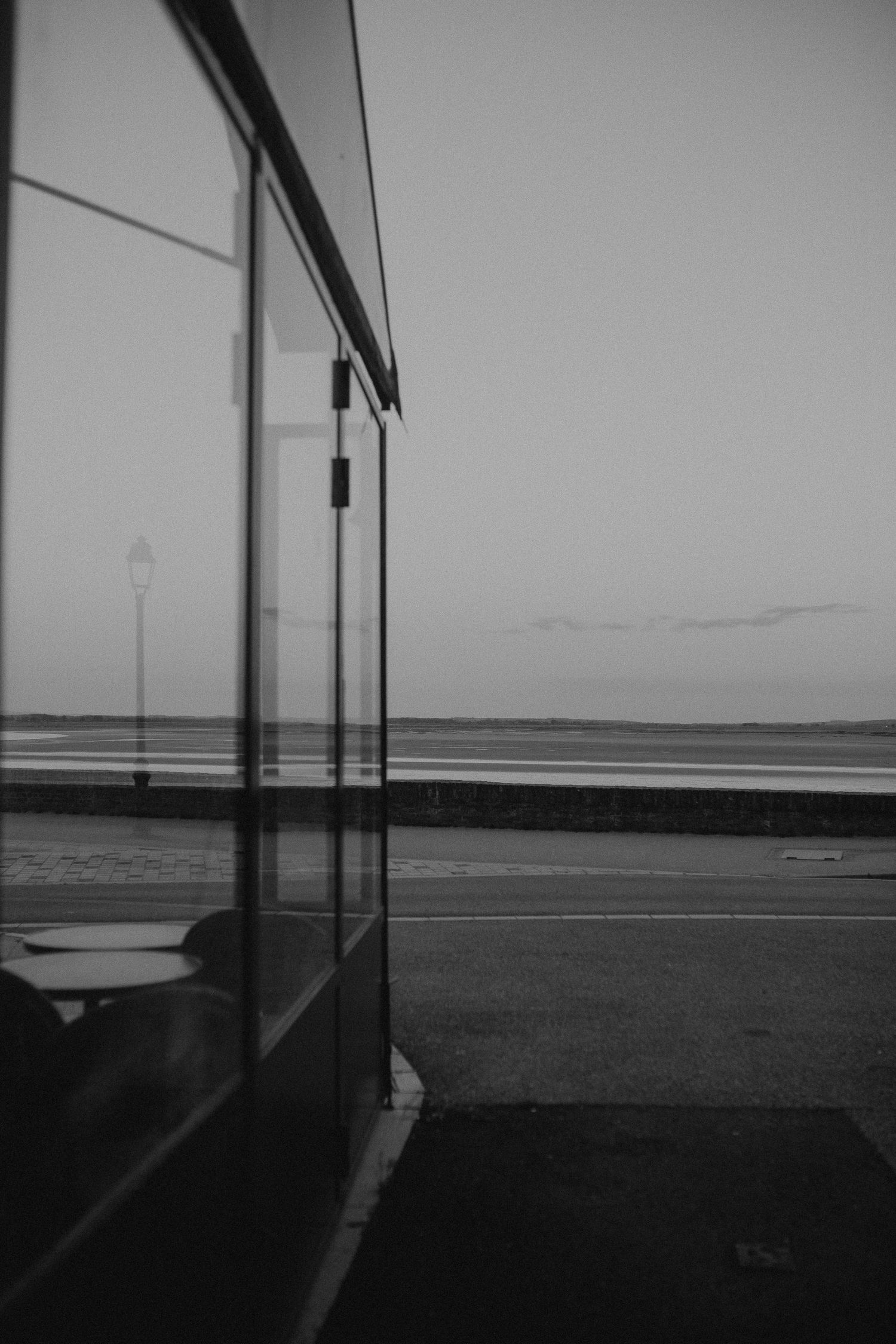 Black and white view of a bus shelter window overlooking a coastal road and ocean on a foggy day.