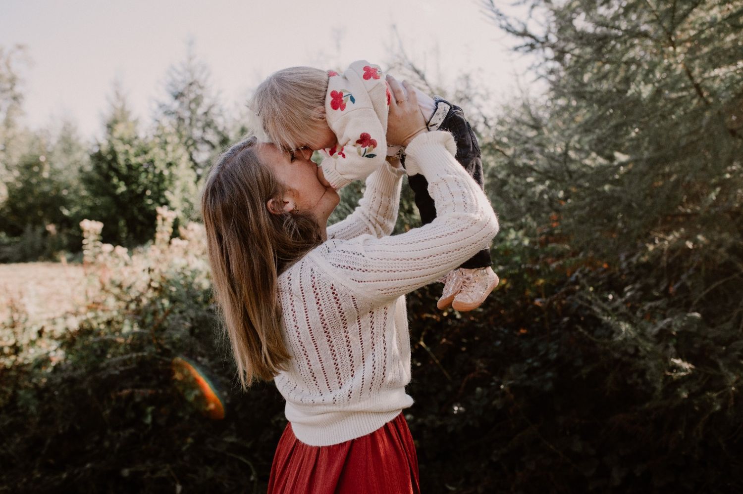 A romantic outdoor photoshoot with a red dress and white sweater against a natural autumn backdrop.