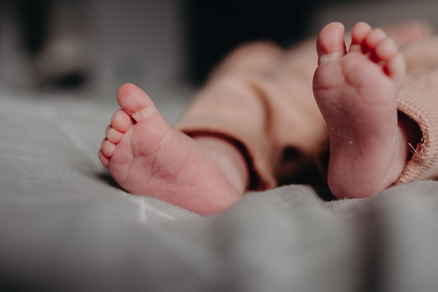 Close-up view of tiny newborn baby feet in soft focus against a blurred background.