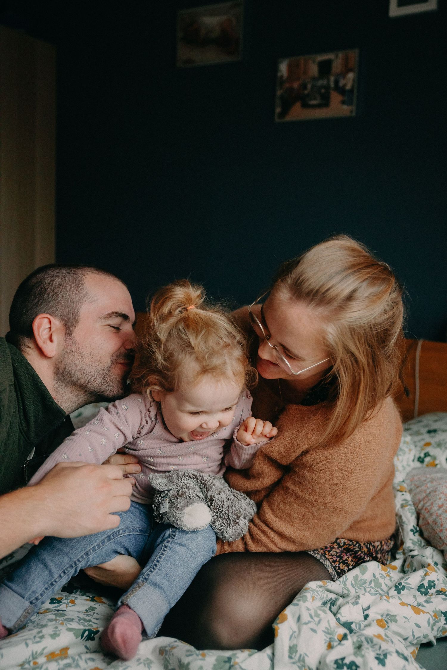 A series of tender family moments showing parents and child cuddling together on floral bedding.