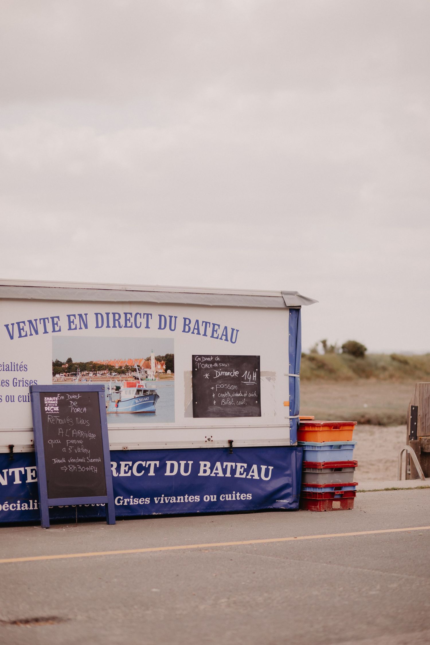 French seafood market stall with 'Vente en direct du bateau' sign and chalkboard menus on a cloudy day.