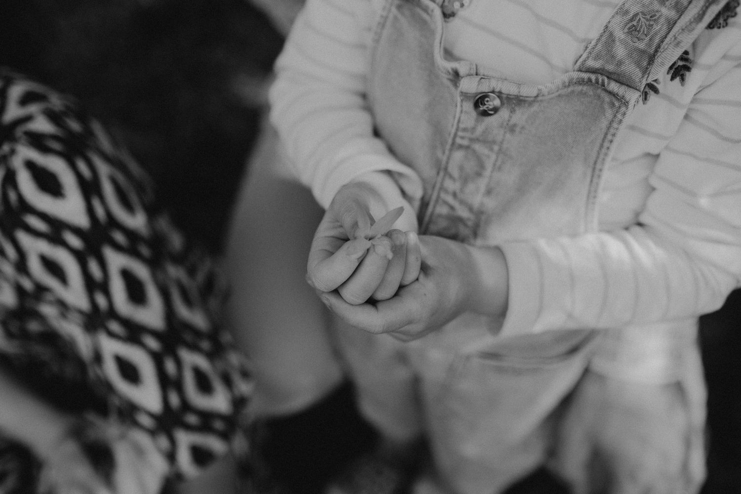 Black and white close-up of hands clasped together while wearing denim overalls and patterned fabric.