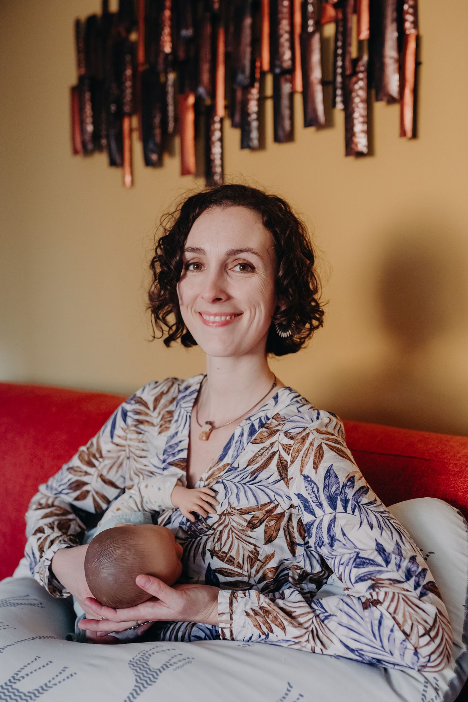 A woman in a floral print dress relaxes on a red couch beneath decorative wall hangings.