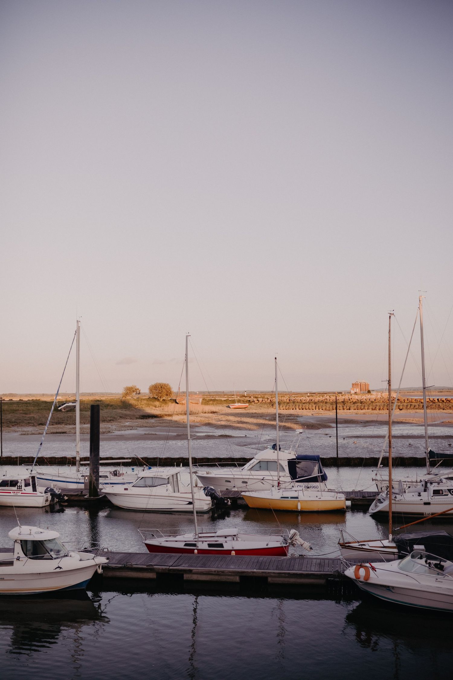 Boats and sailboats docked in a marina at sunset with calm waters reflecting the peaceful evening sky.