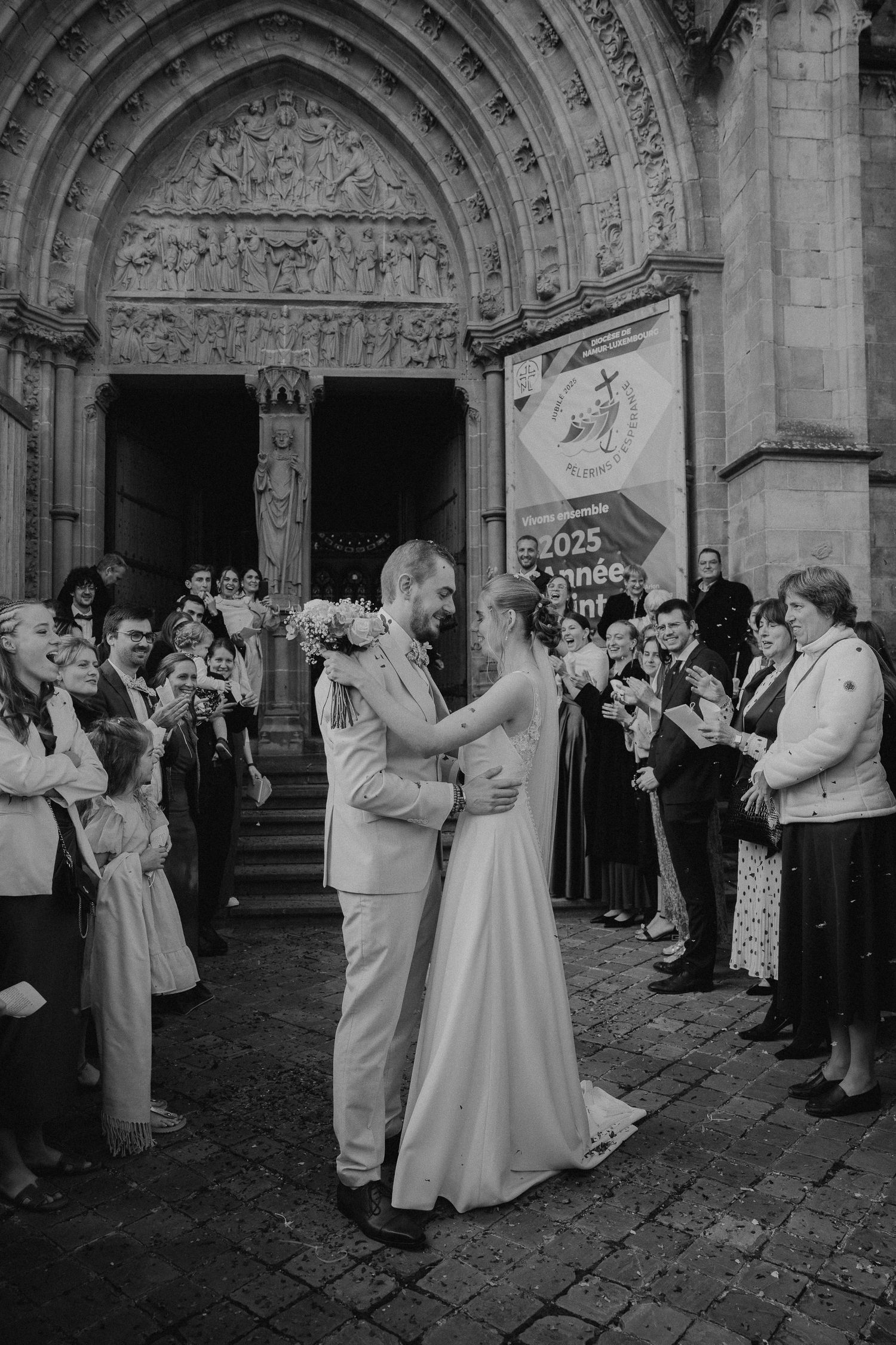 Wedding party and guests lined up outside a grand cathedral with ornate stone archways.