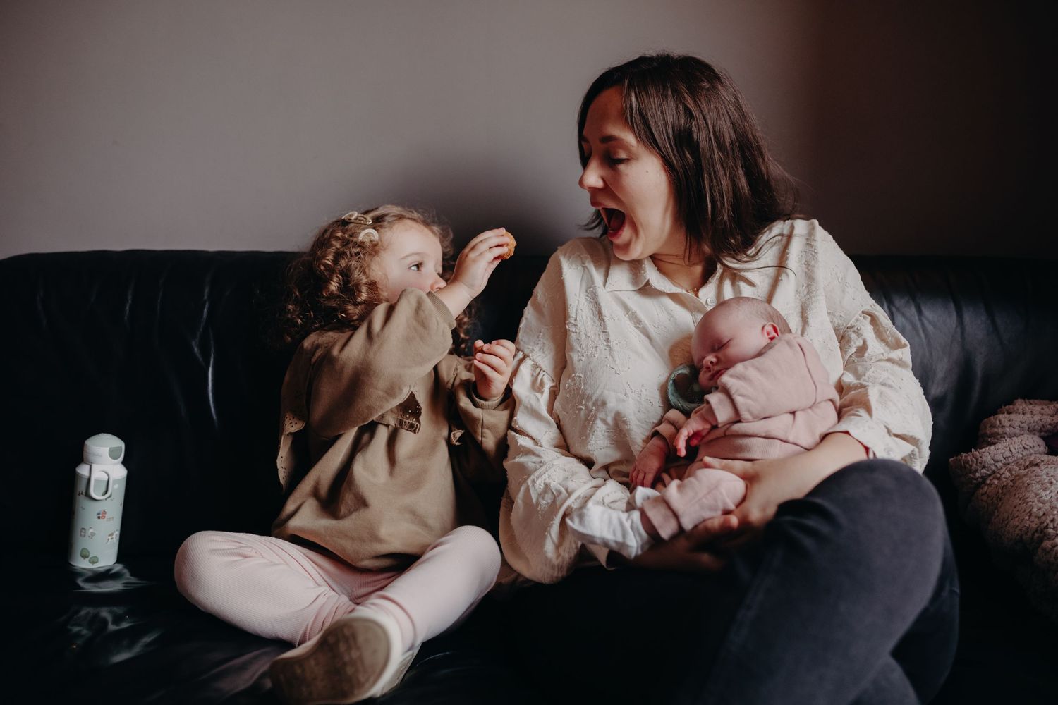 A parent and toddler share a joyful moment while sitting together on a dark leather couch.