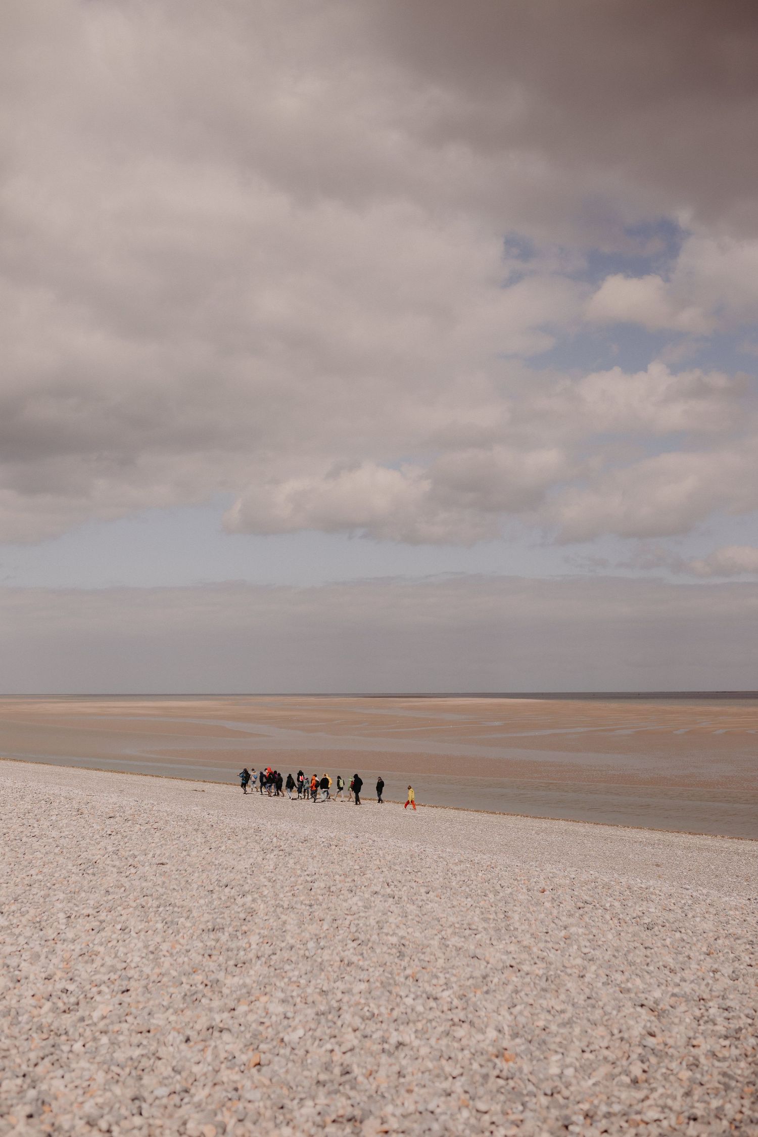 A group of distant people stand on a salt flat under dramatic cloudy skies creating a stark desert landscape.