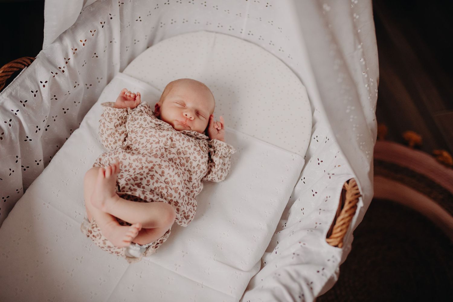 Newborn baby sleeping peacefully in white bassinet wearing cozy beige knit outfit.