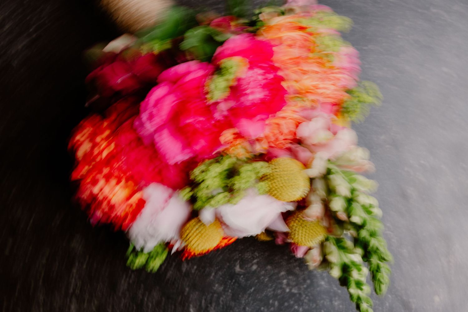 Blurred motion shot of vibrant pink, red, and green flowers creating an abstract colorful swirl on a dark background.