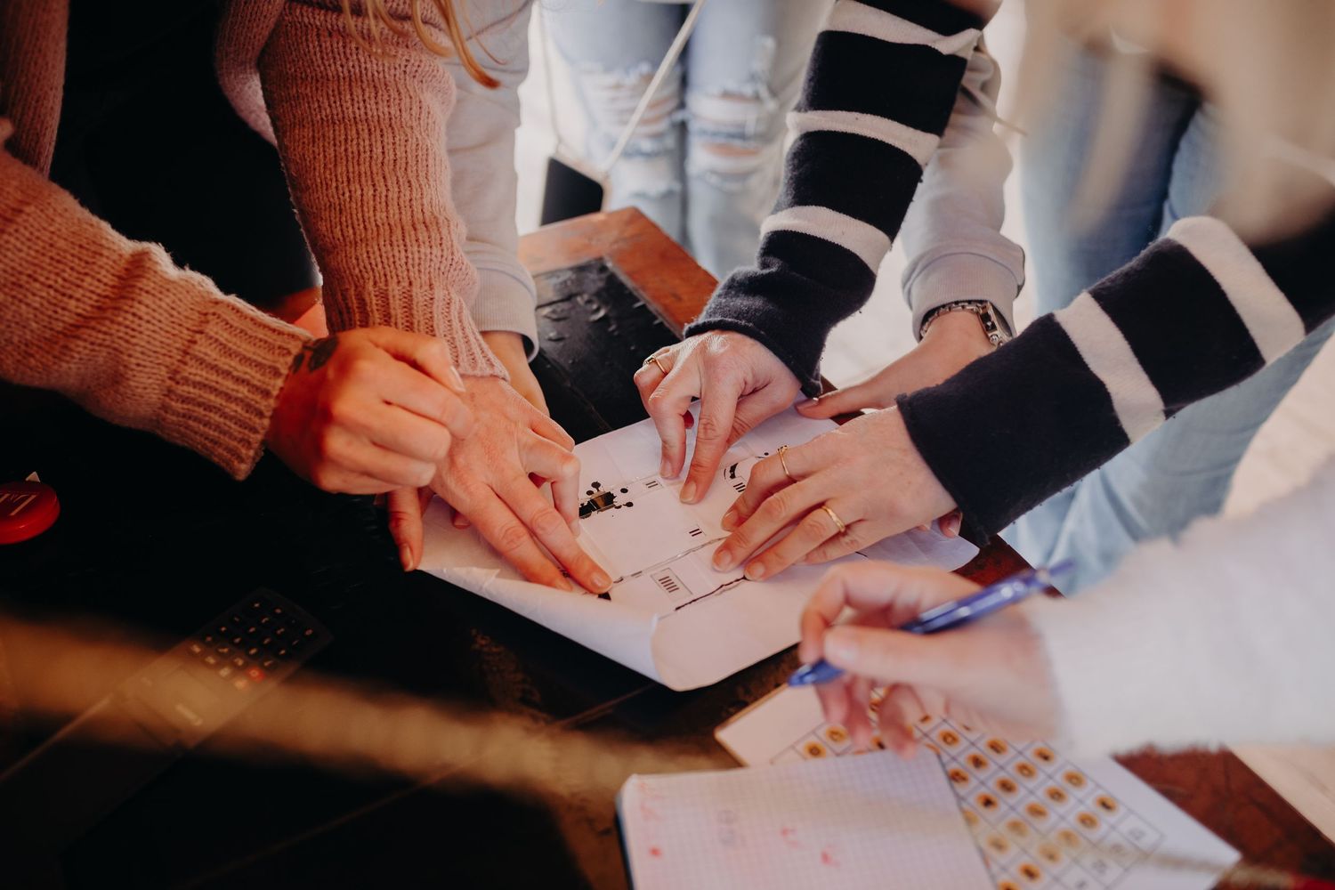Multiple hands collaborating together on paper documents and planning materials spread across a table.