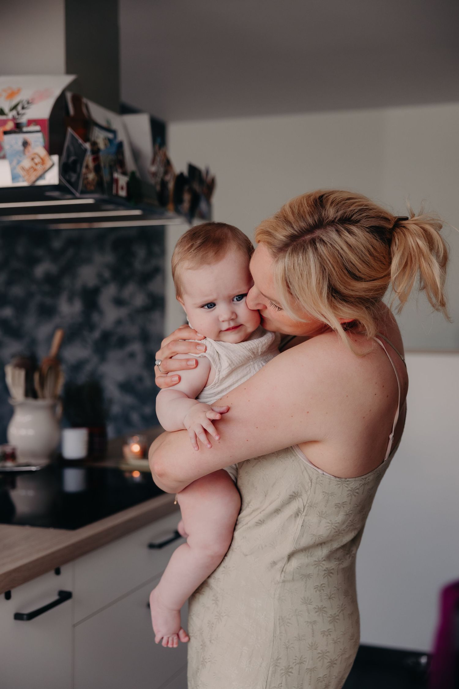 A tender moment between parent and baby is captured in a series of candid photographs in a modern kitchen setting.