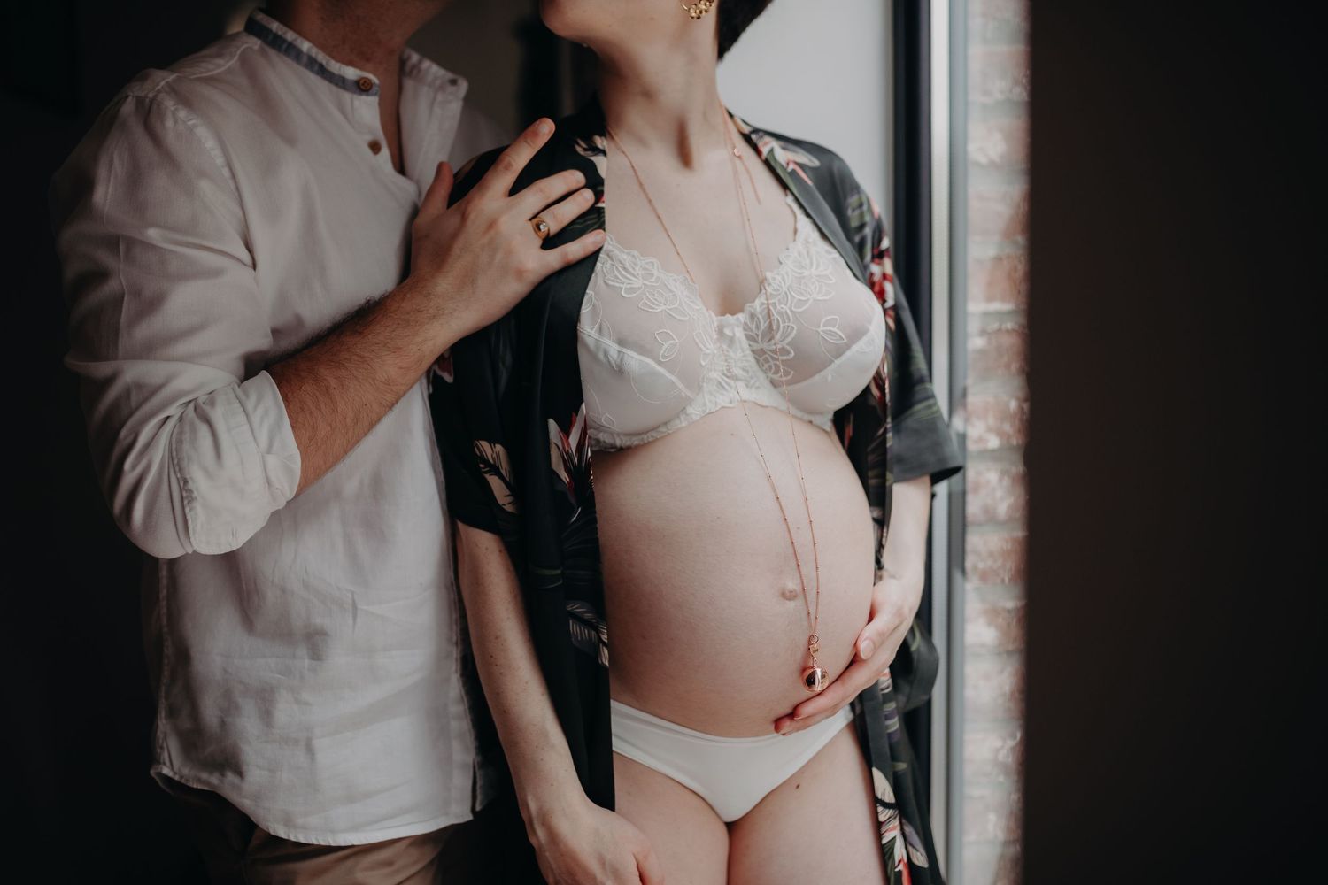 Intimate maternity photography series showing silhouettes of a couple embracing in romantic poses against dark backdrop.