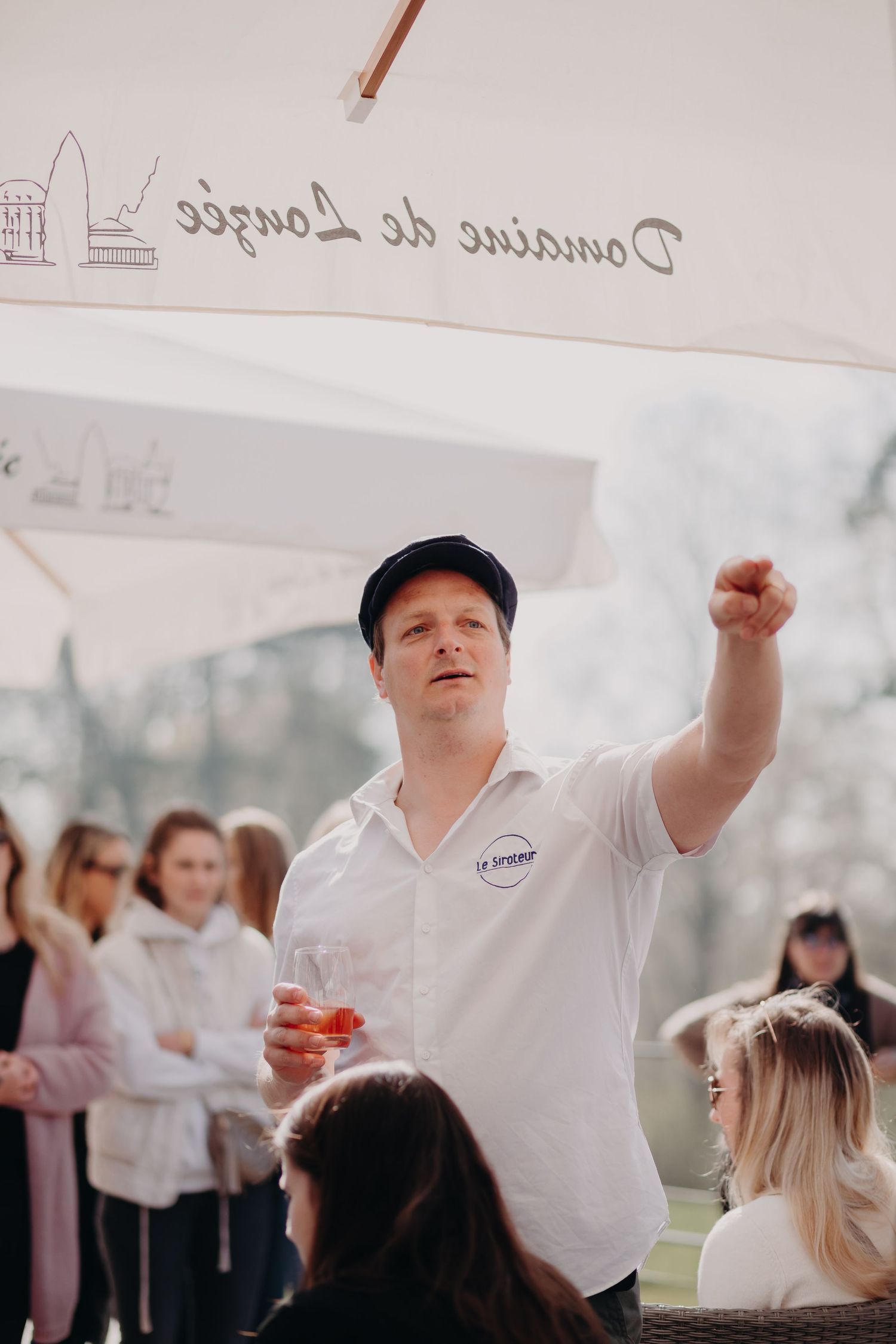 Someone wearing a white shirt and cap gestures while speaking to a crowd during an outdoor event.