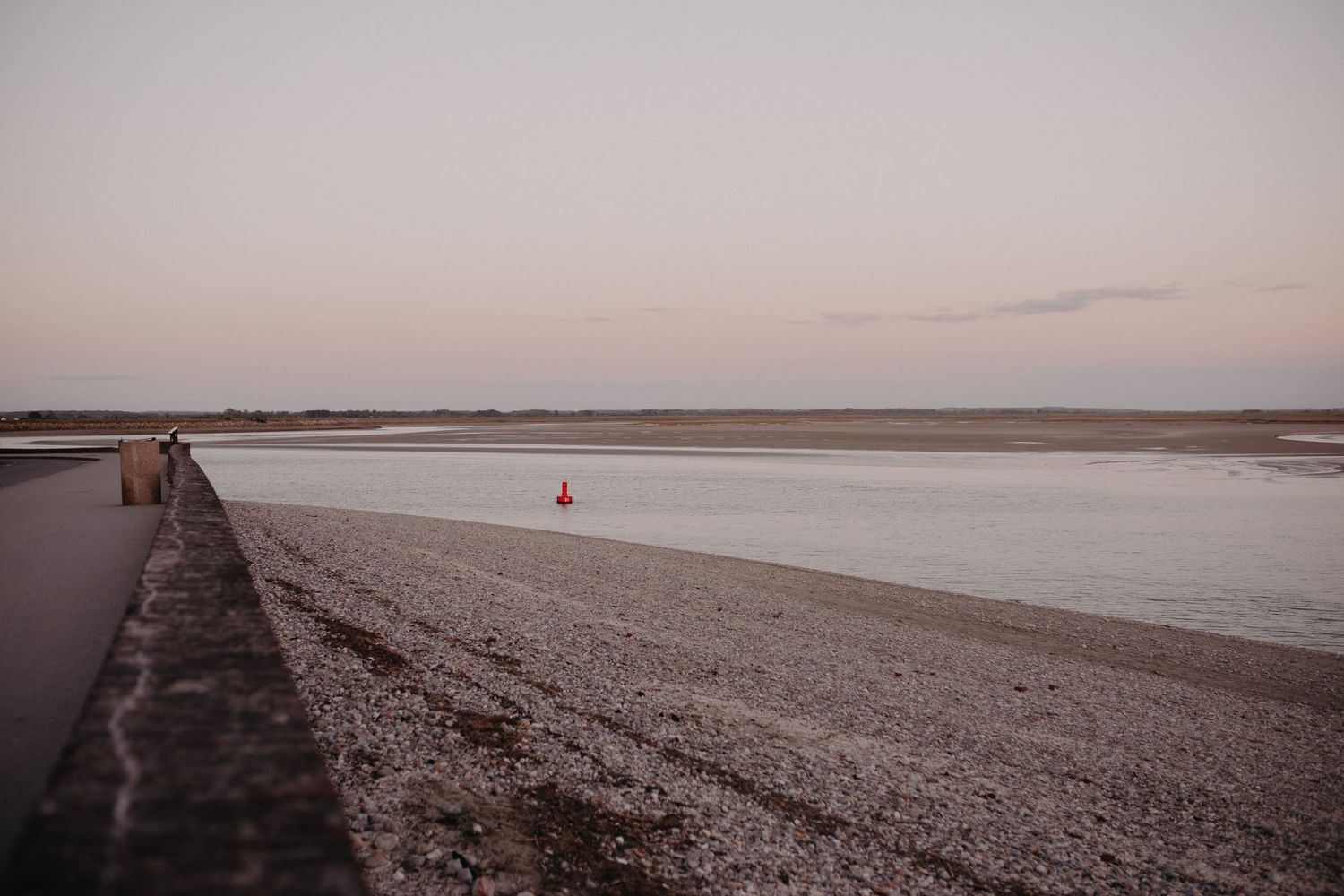A lone seagull stands on an empty beach during sunset with a stone pathway extending into the distance.