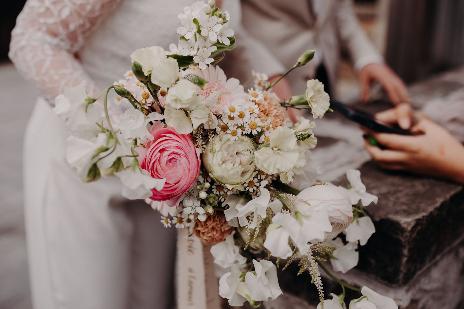 A romantic wedding bouquet with pink roses, white flowers and delicate baby's breath against a soft blurred background.