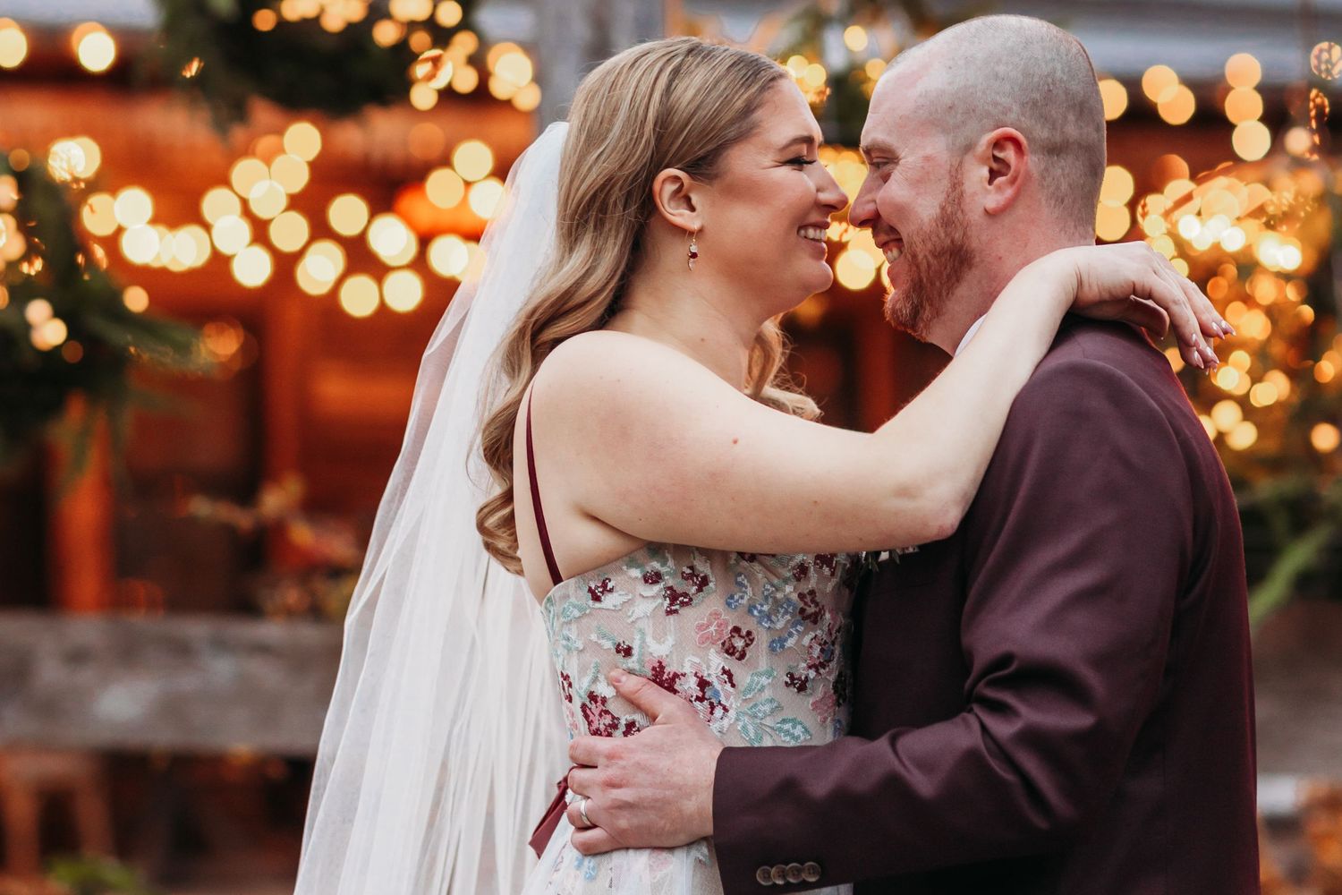 Couple kissing beneath glowing string lights in the evening.