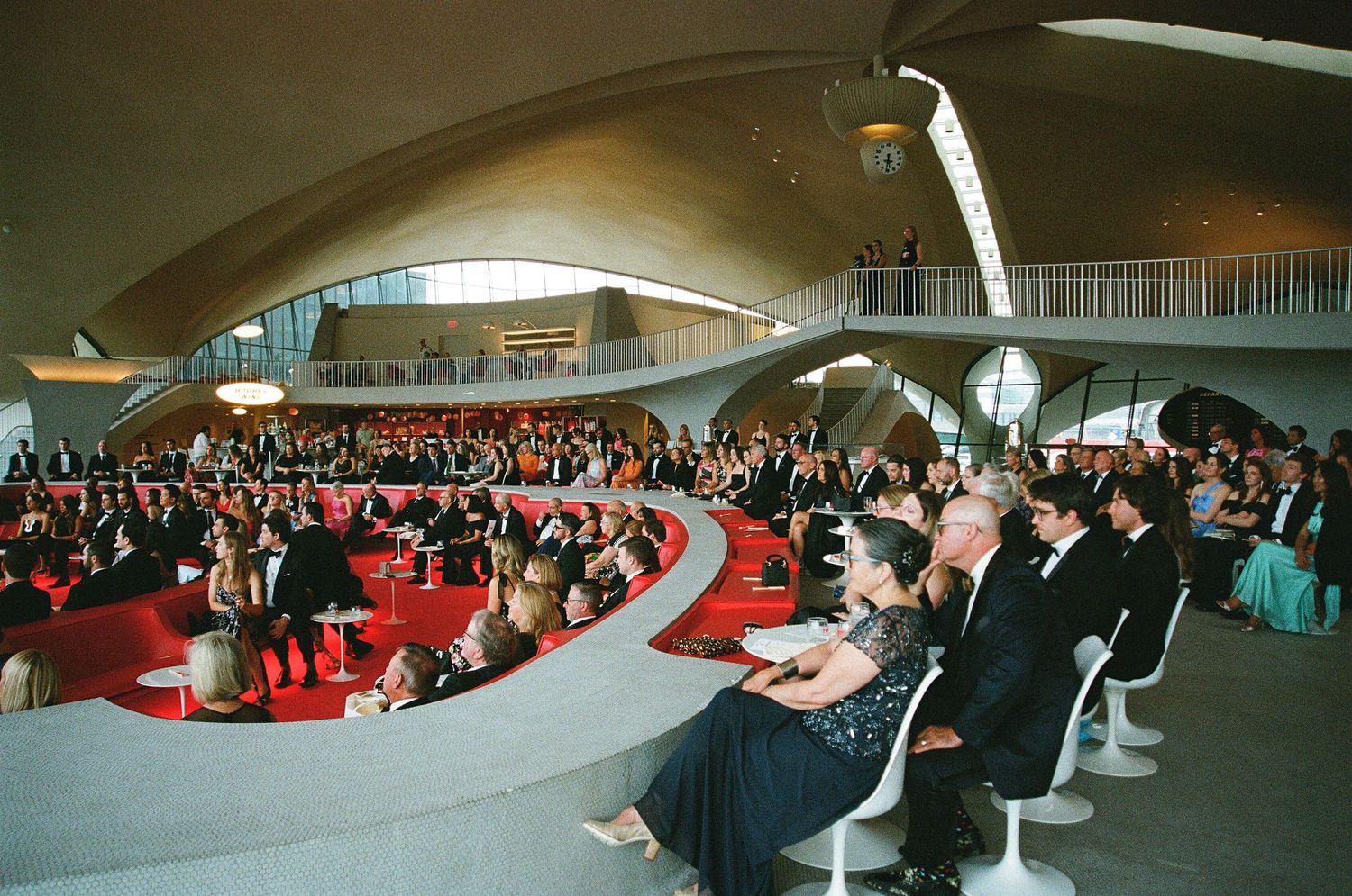 Sweeping wide-angle wedding ceremony beneath dramatic curved mid-century architecture, captured on film.