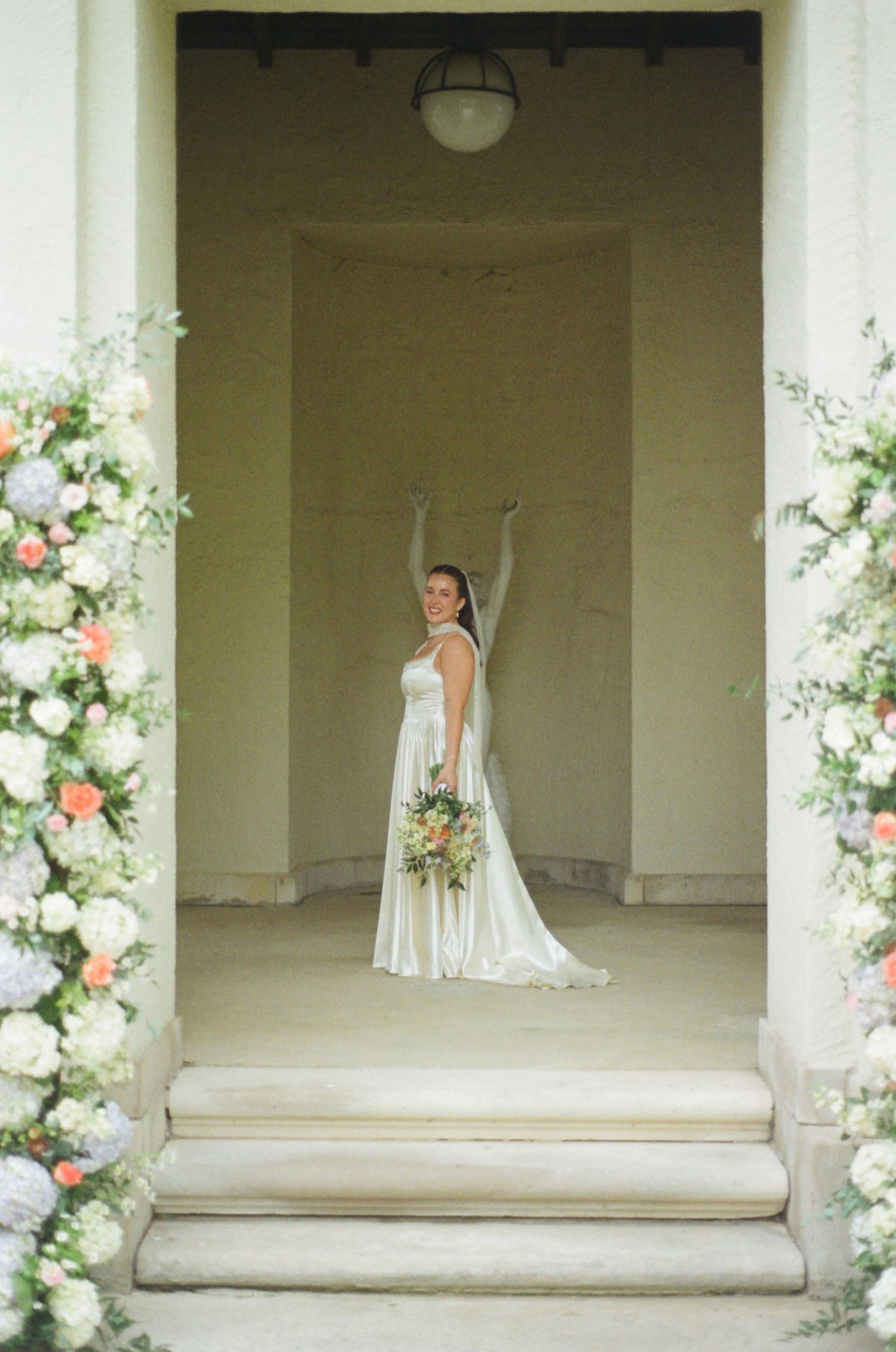 Bride framed in a doorway surrounded by greenery and white floral arrangements.