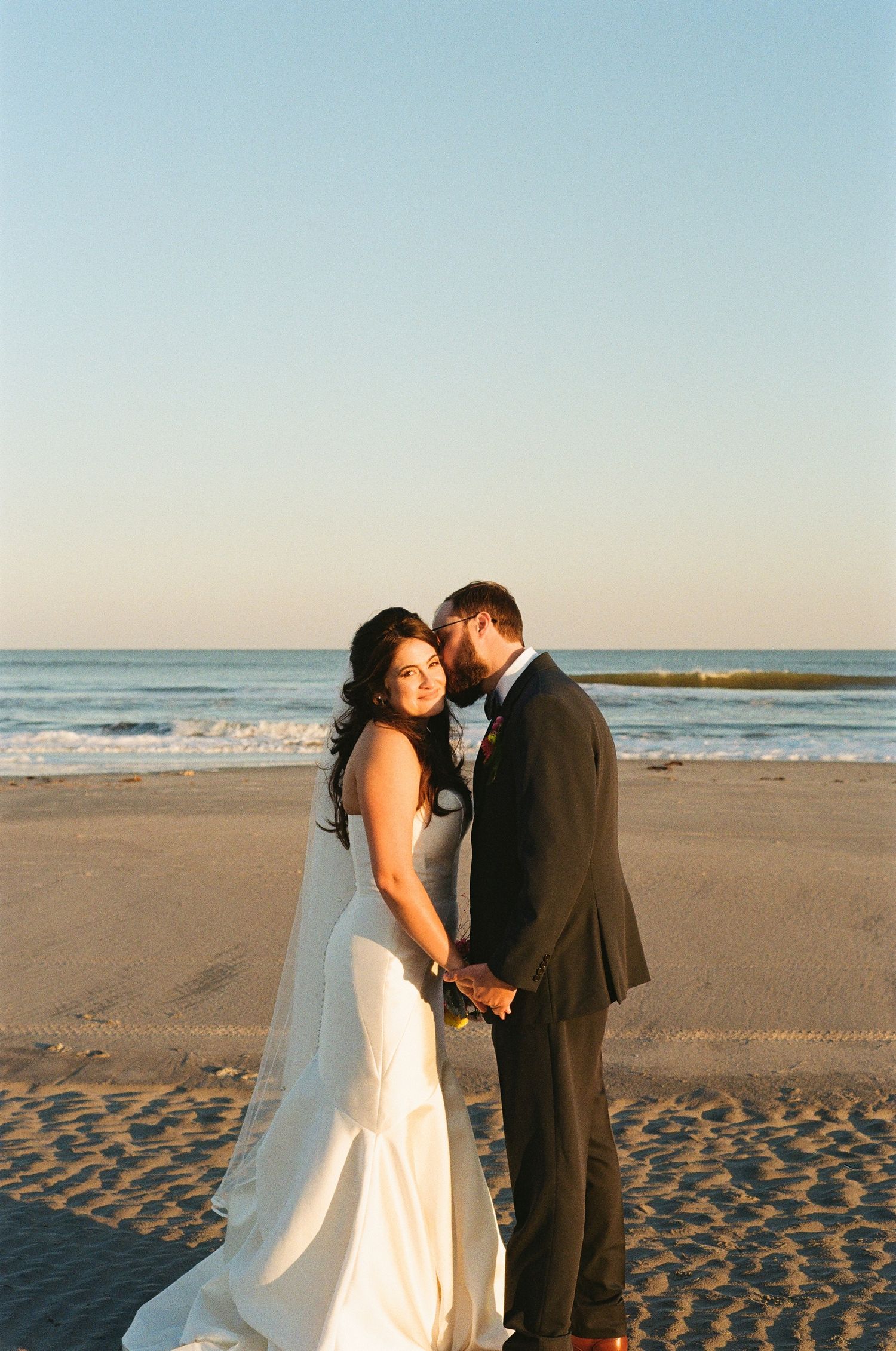 Bride and groom standing close together on the sand during a beach elopement at sunset.