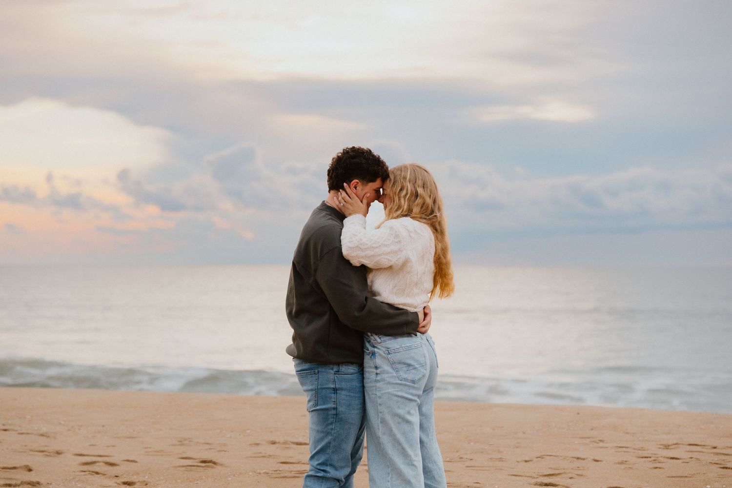 Couple holding each other on the sand at sunset during a beach engagement session.
