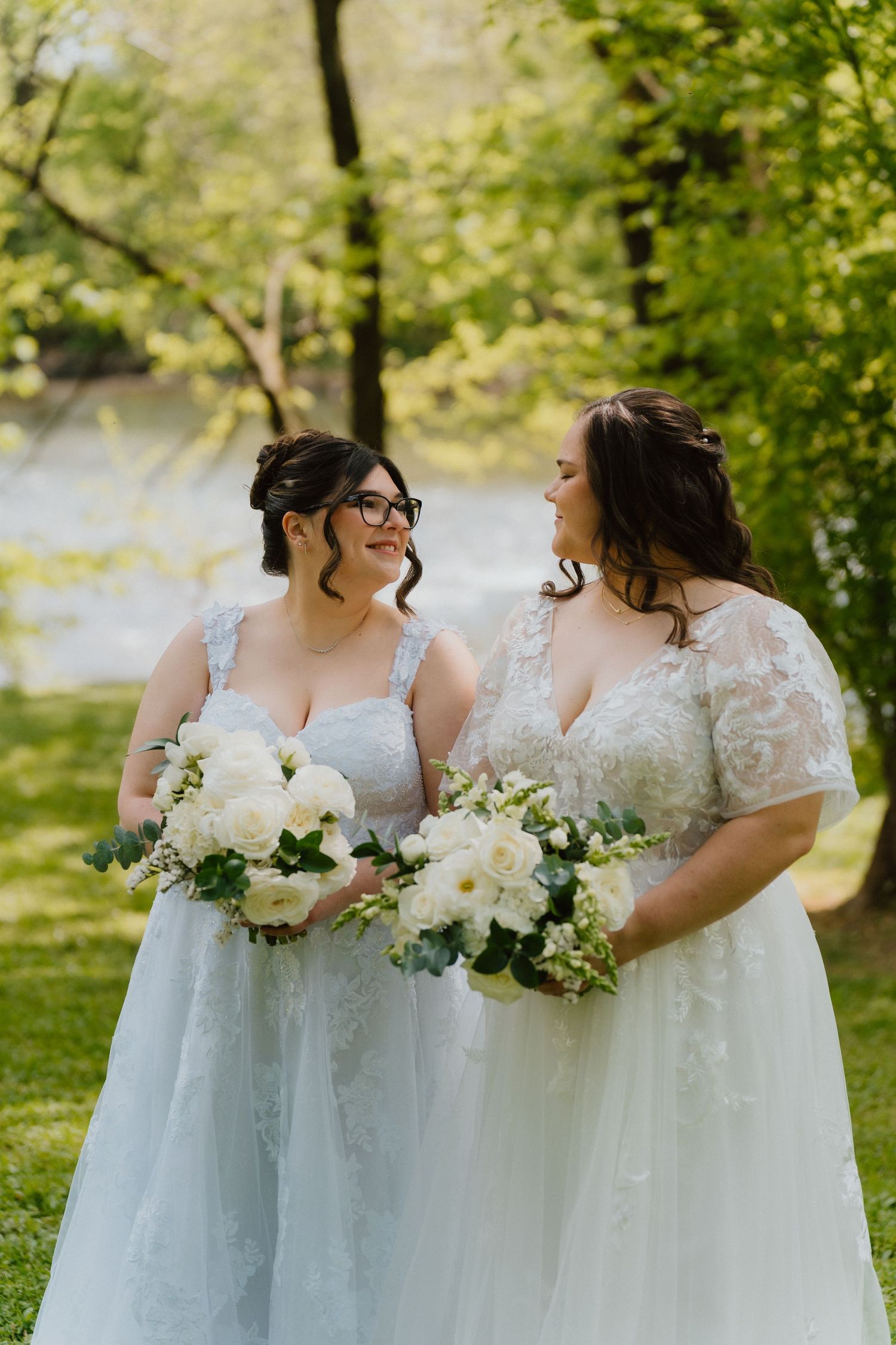 Two brides holding bouquets in a garden during an outdoor wedding.