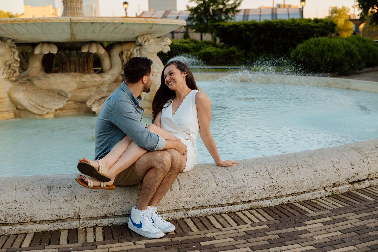 Couple crouching beside a poolside fountain at a resort.