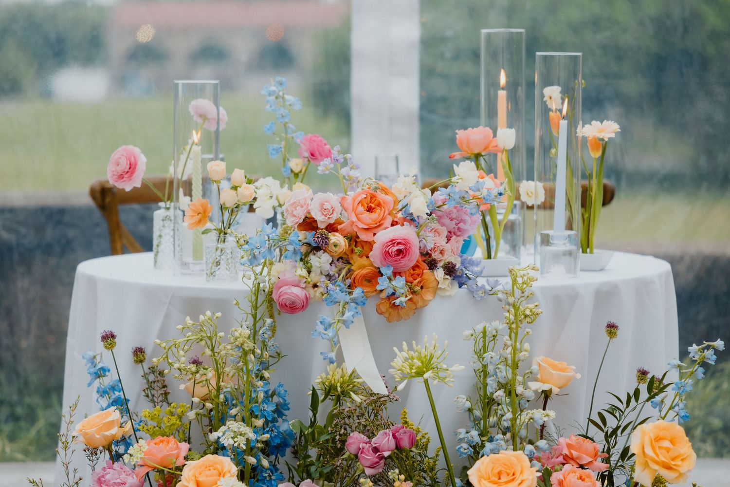 Sweetheart table adorned with colorful florals and candles at an outdoor reception.