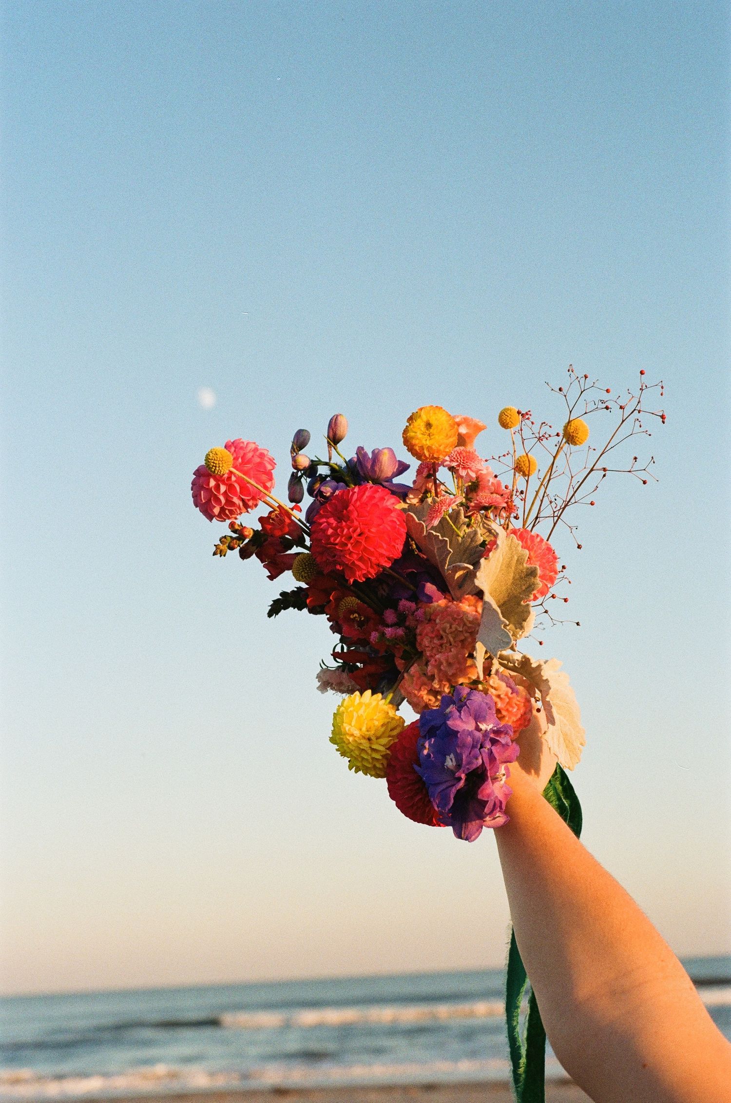 Hand holding a colorful wildflower bouquet on the beach during a coastal elopement.