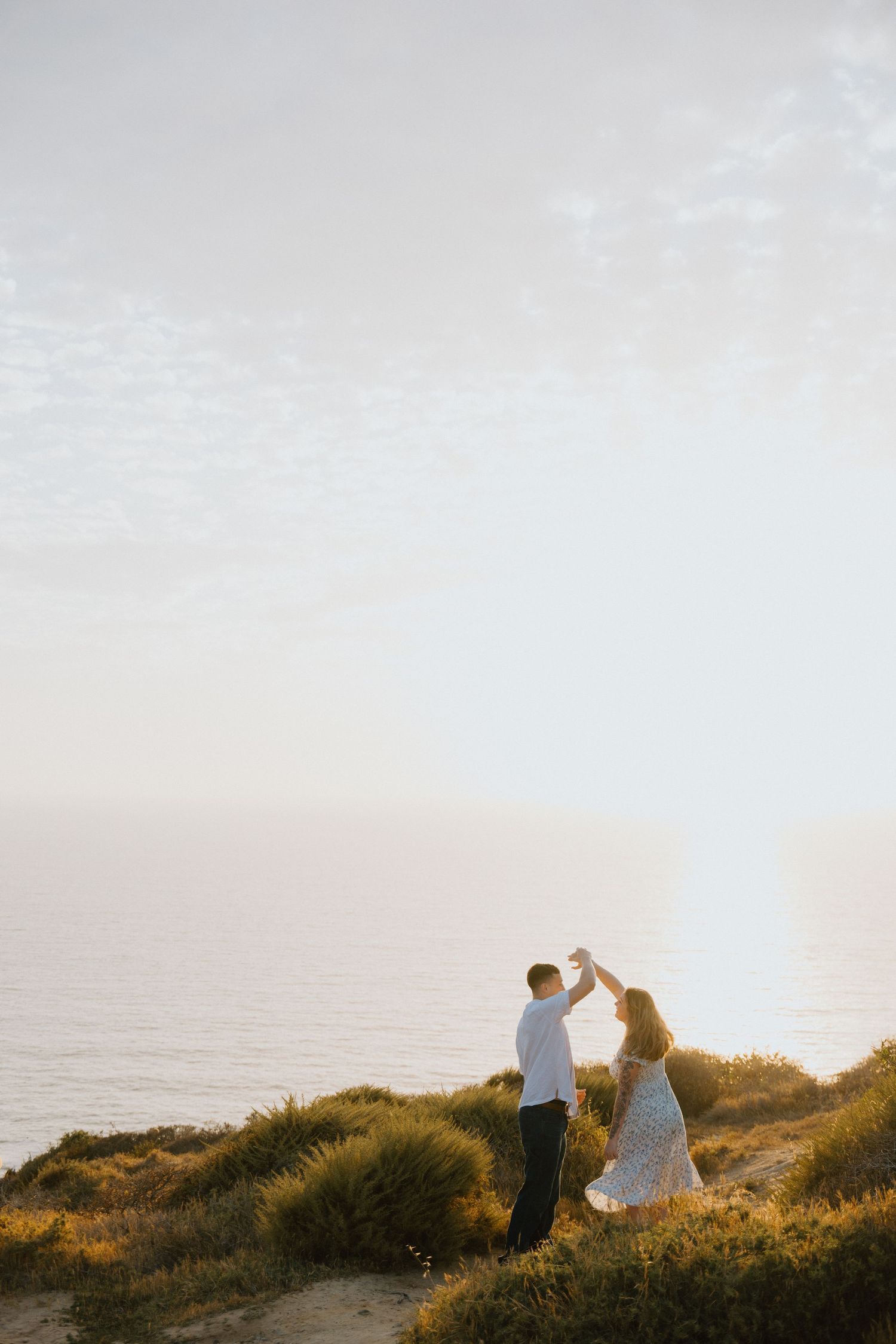 Couple embracing on a grassy bluff above the ocean at sunset during a coastal elopement.