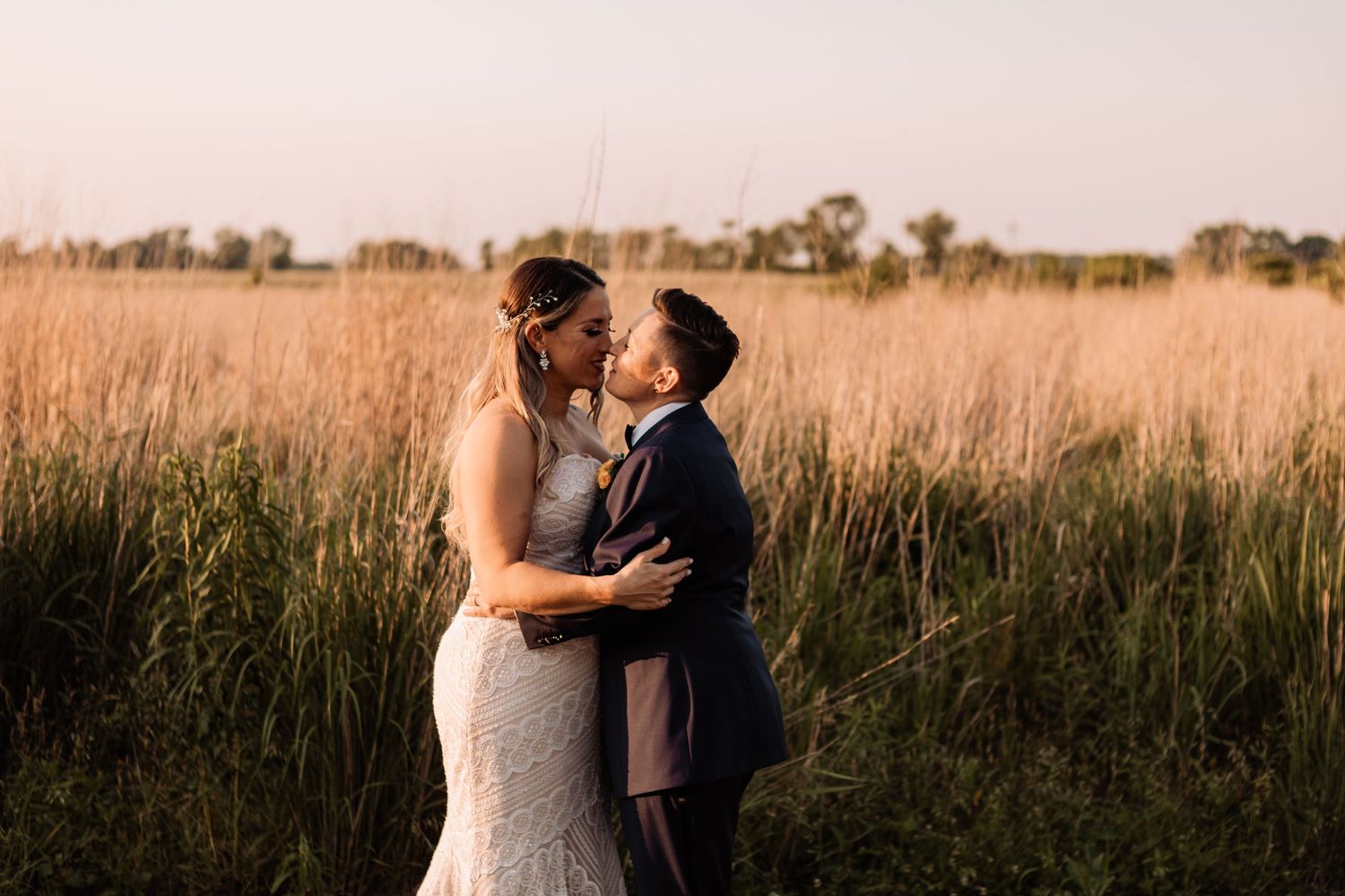 Bride and groom kissing in a tall grass field at sunset during a countryside wedding.