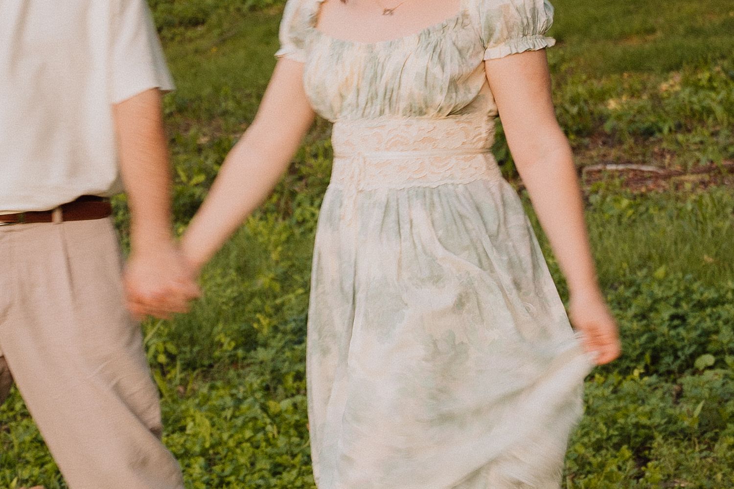 Couple holding hands in a grassy meadow.